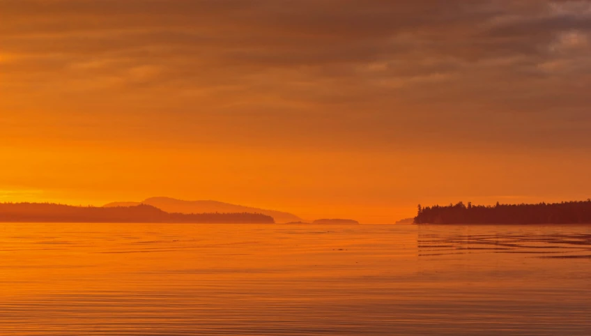 a view from the water as the sun rises over some land