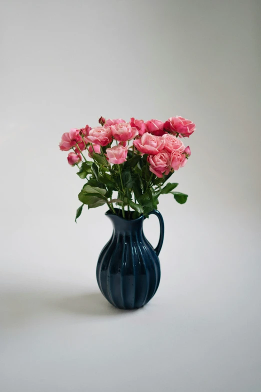 several pink roses in a blue vase on a white table