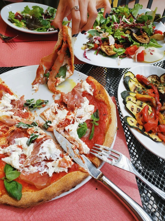 people holding utensils with their hands to a pizza on the table