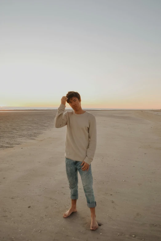 a man wearing jeans and a sweater standing on the beach