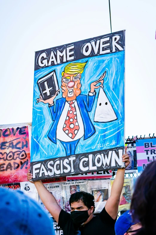 a man holding up a sign that reads game over and an cartoon of donald the trump