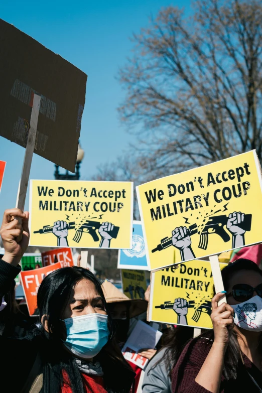 people with masks holding up signs that say we don't accept military coups