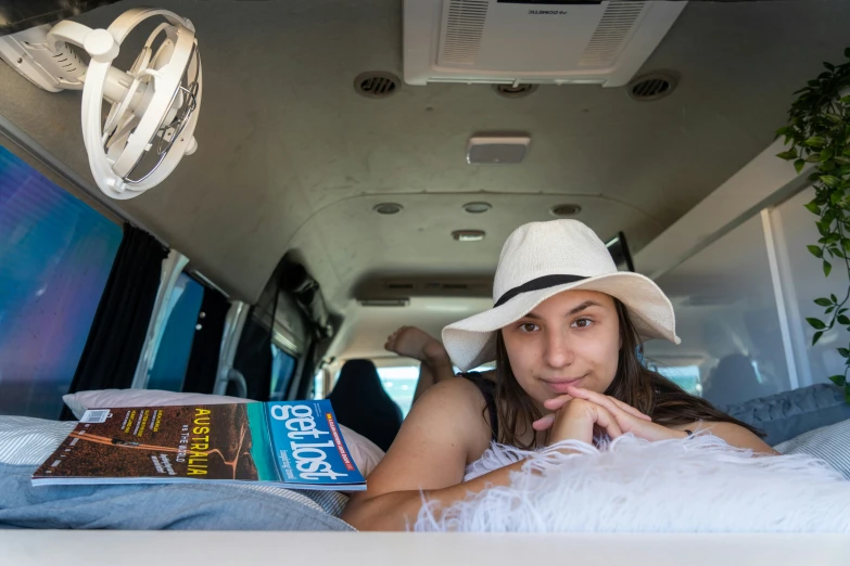 a girl wearing a hat is reading in the back of a van