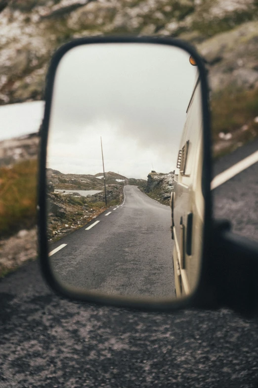 a side view mirror is seen with a road in the reflection