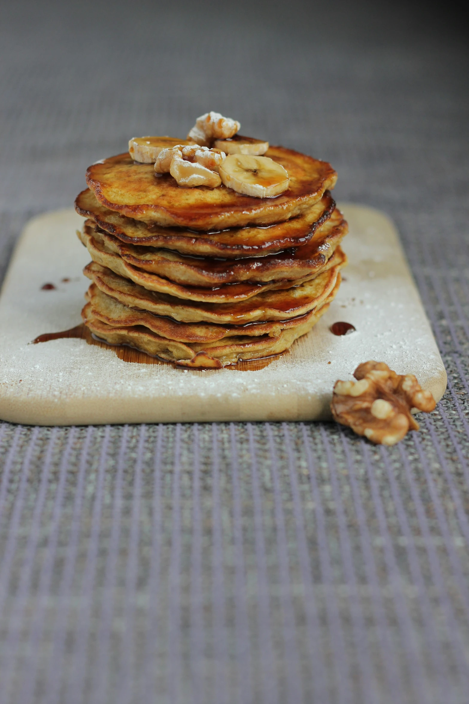 a stack of sliced bananas sit next to nuts on a wooden plate