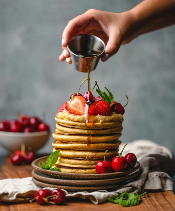 someone pouring syrup onto some stacked pancakes