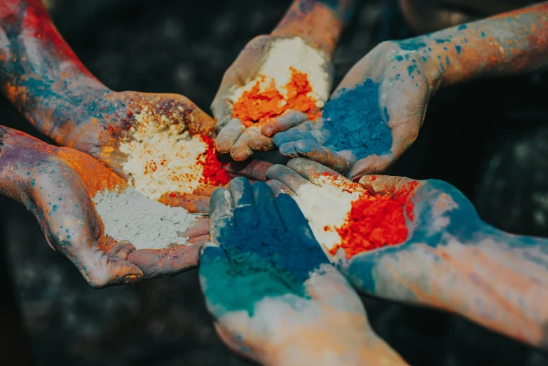 many hands in colorful powder and mud with a white bowl