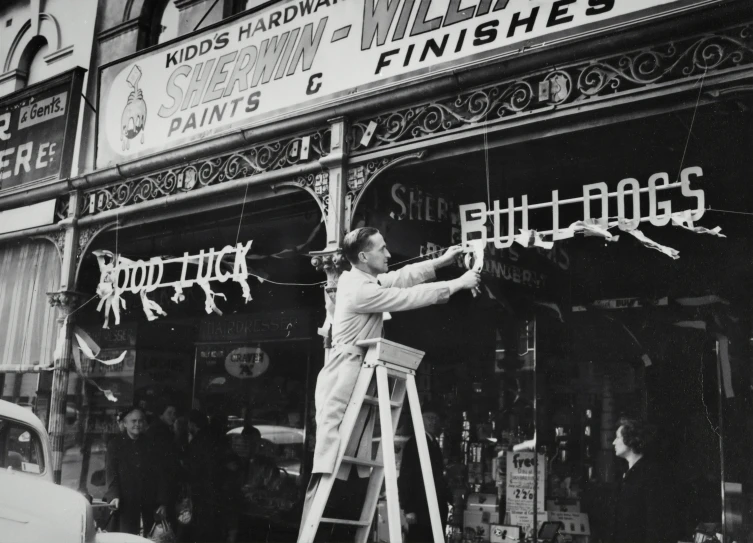 a man standing on a ladder holding a paint brush in front of a shop