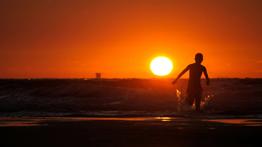 the sun is setting over the ocean with a surfer