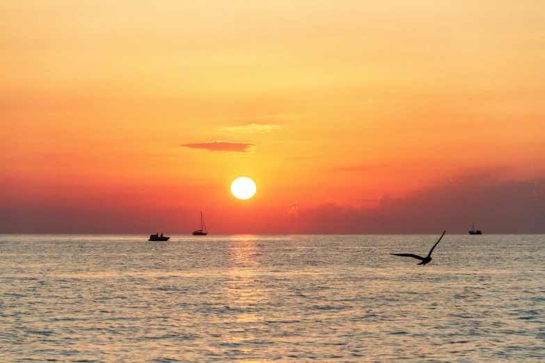 the sun is setting over the water with three small boats