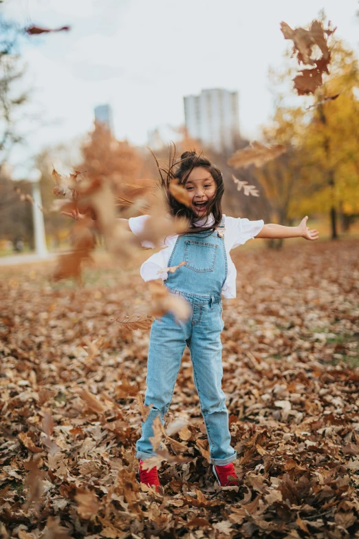 a little girl is jumping in the air in the leaves