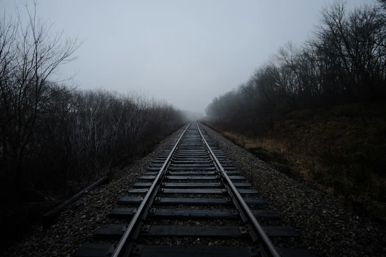 an old railroad track with the sky covered in fog