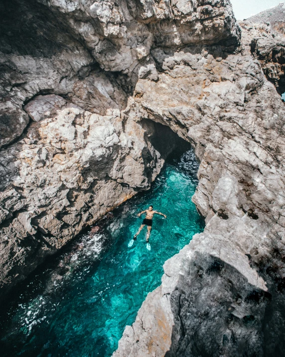 person swimming in a pool between two cliffs