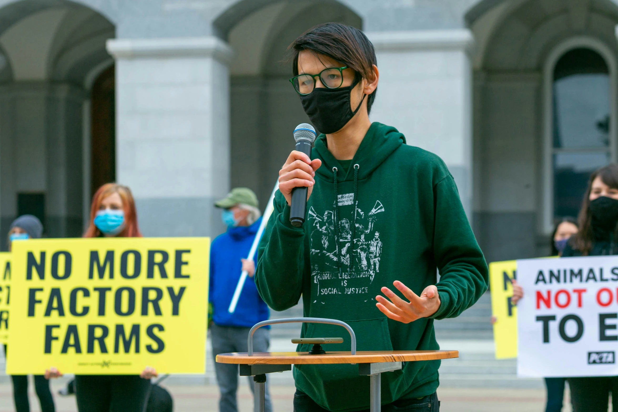 protester wearing a mask holding microphone standing behind table with signs