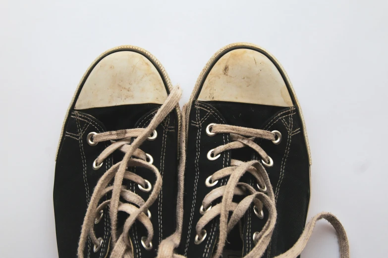 an old pair of black shoes with tan laces and a worn sole