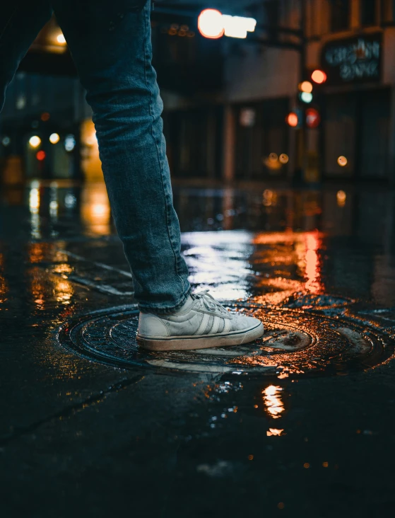 a close up of a person wearing white tennis shoes standing on a rain covered sidewalk