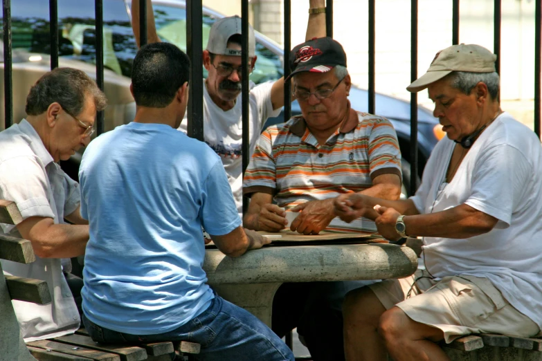 four men playing cards while seated at table outside