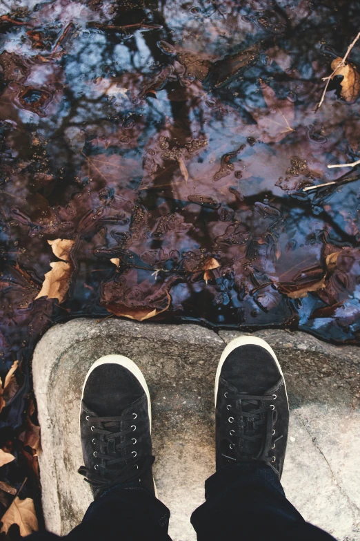 a persons legs standing near a small stream of water