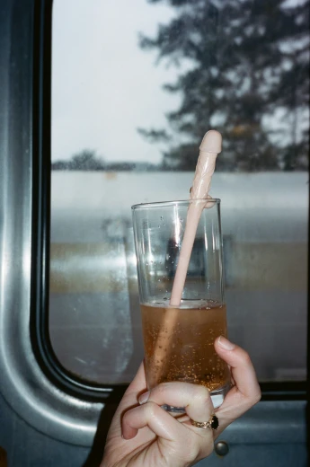a person holds up a glass of liquid and an object