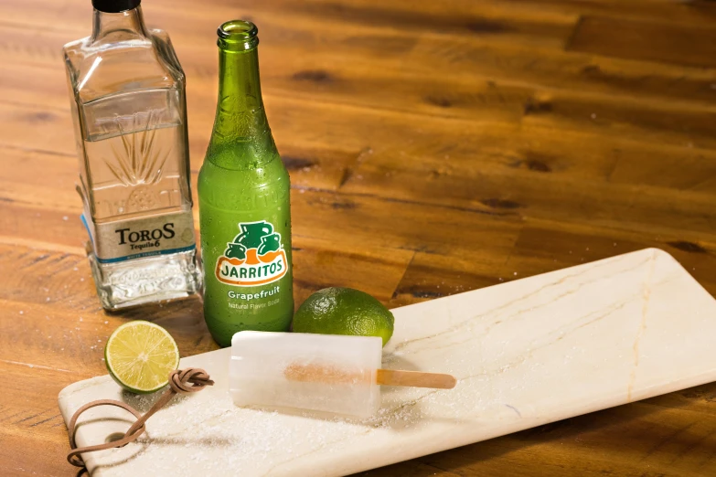 a bottle and some limes are on a  board