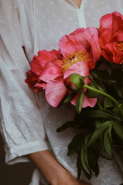 pink flowers are held in the hands of a woman