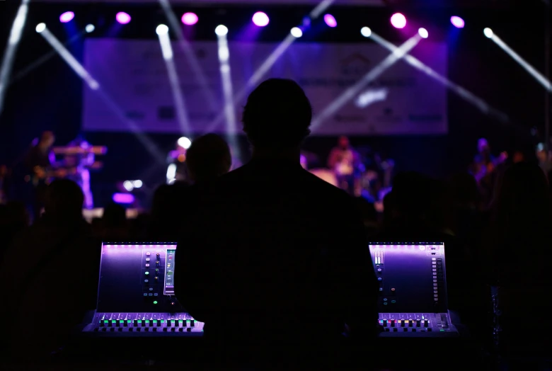 two laptops are on a dark stage as a performer is in the background