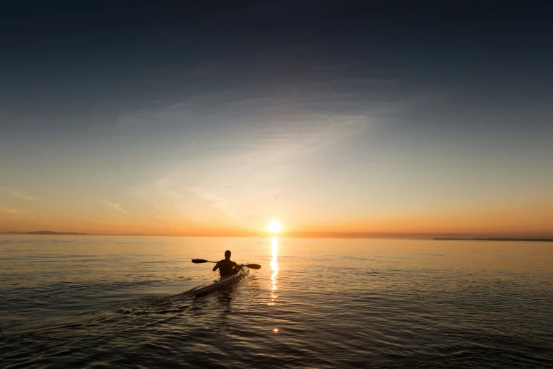 a person paddling on a surfboard at sunset