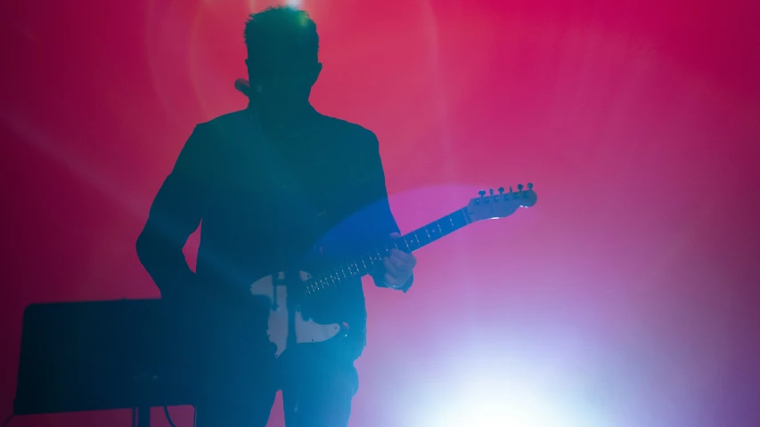 silhouetted guitarist with instrument in front of red background