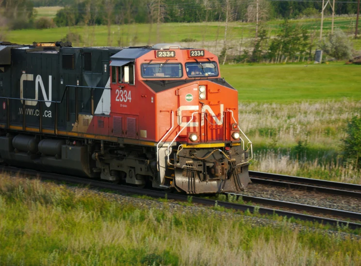 an orange engine with black and red containers is moving down the track