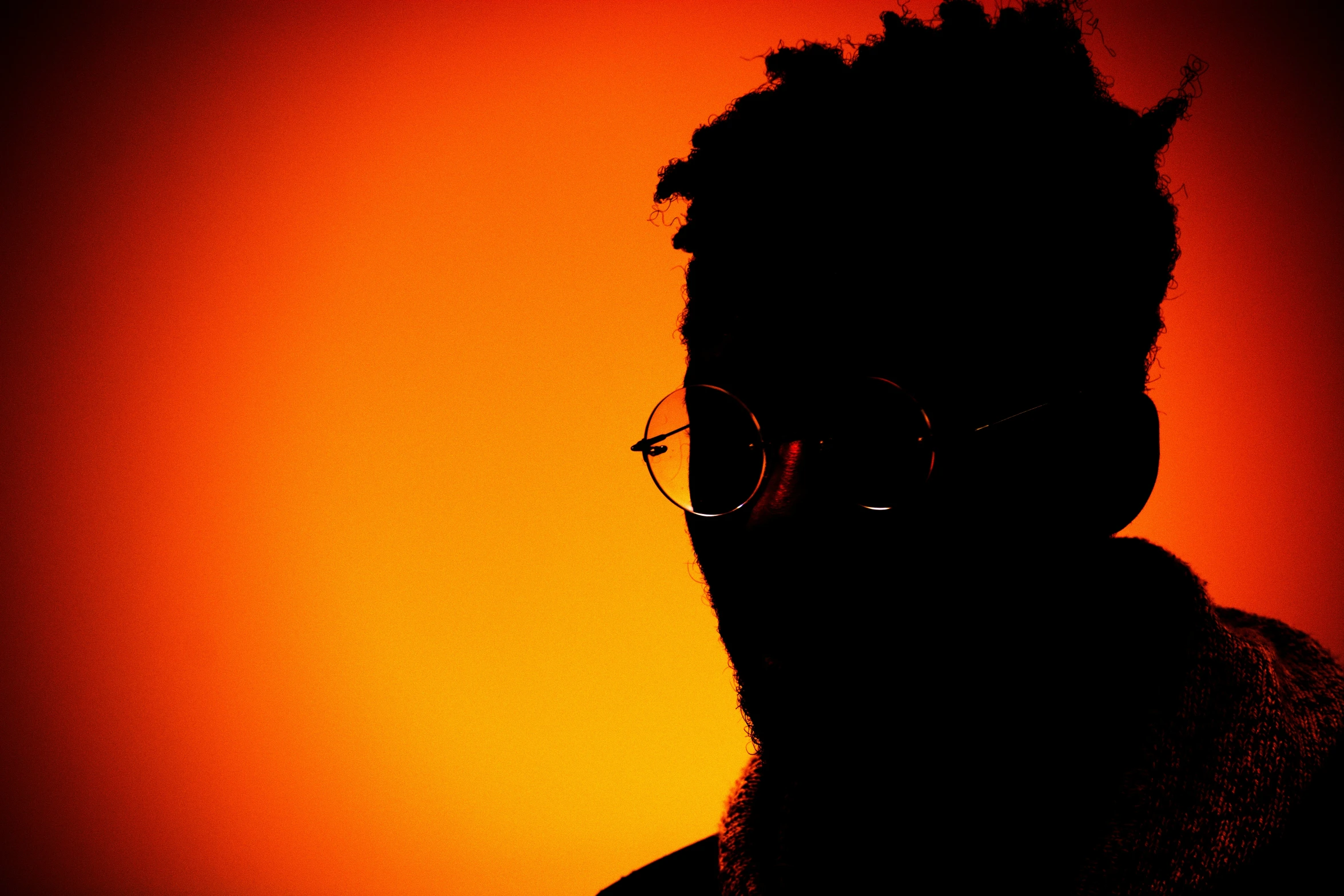 a man with a beard and eye glasses in front of an orange sky
