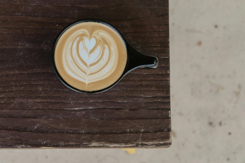 a cappuccino with a pattern on top sits atop a wood surface