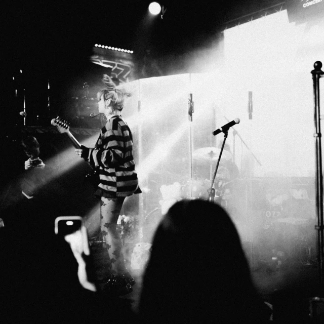 the band perform a song while a speaker stands behind them