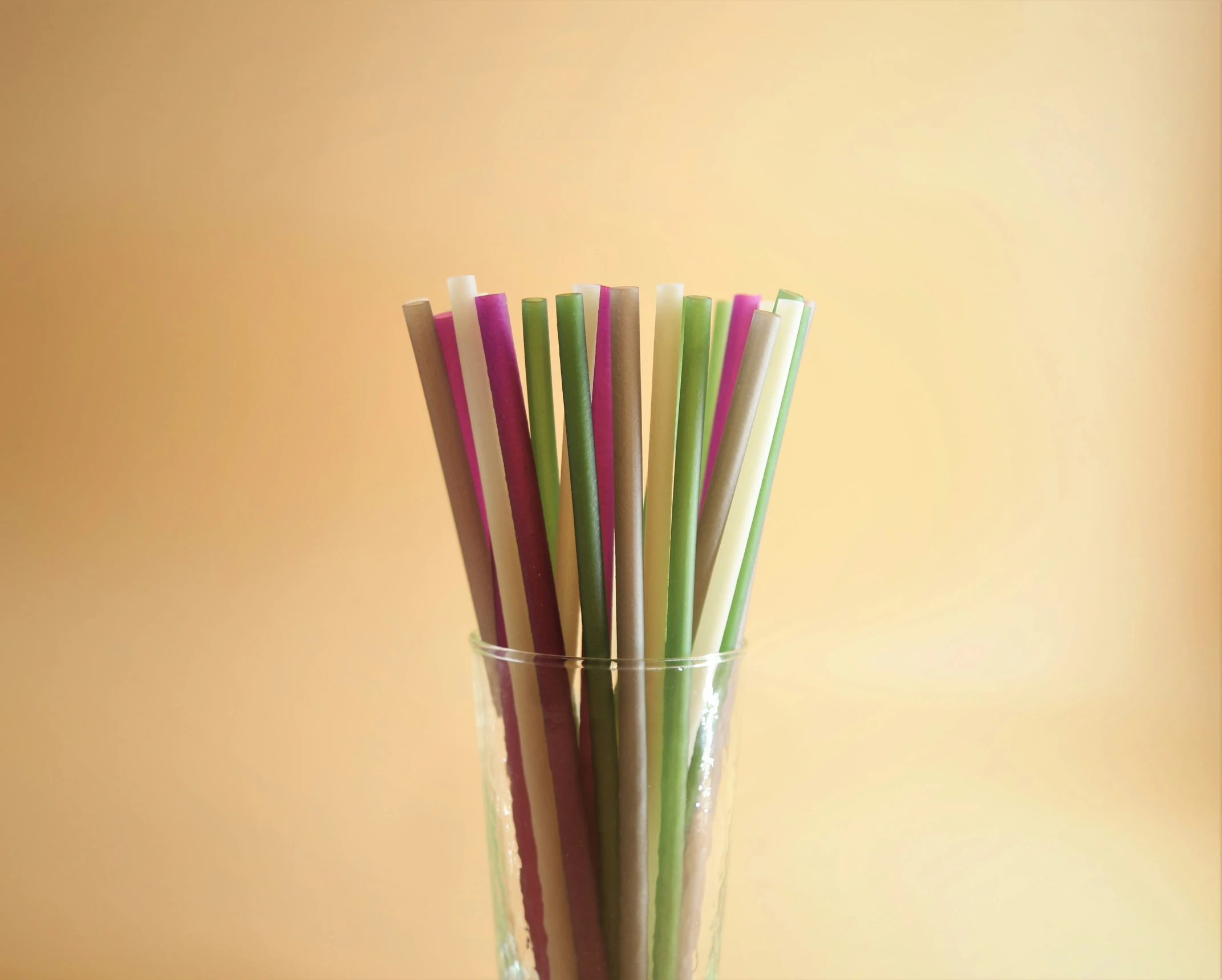 colorful straws in a clear glass against a yellow background