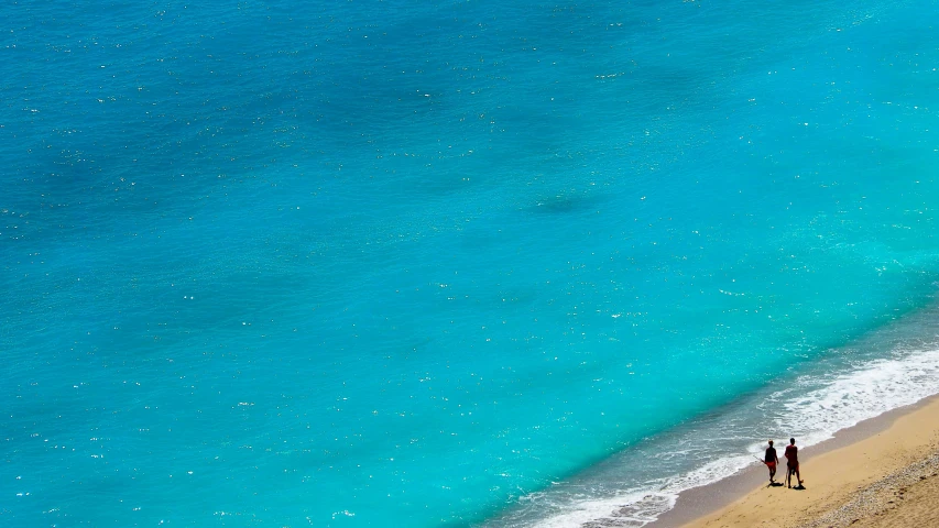 two people are standing on a beach by the water