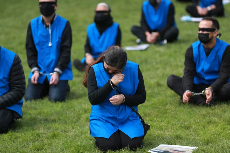 a group of people wearing blue vests sitting in grass