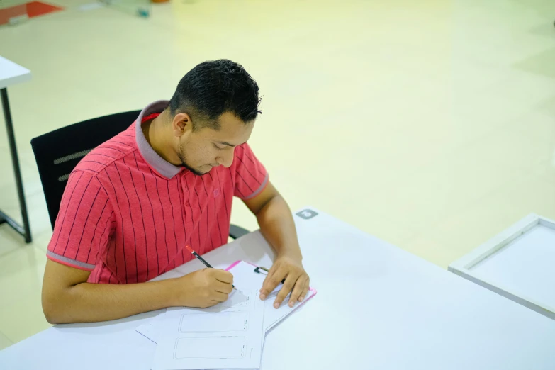 a man in a red shirt is writing on some paper