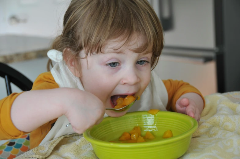 a little boy eating food from a green bowl