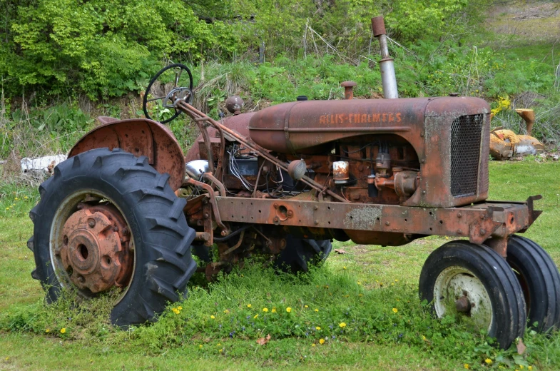 a rusty old farmall on grass near trees and hills