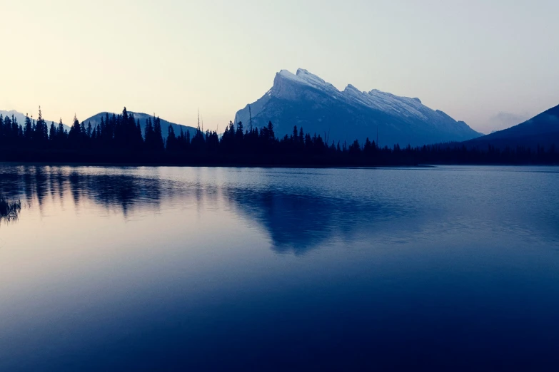 the silhouette of a mountain and trees reflects in the water