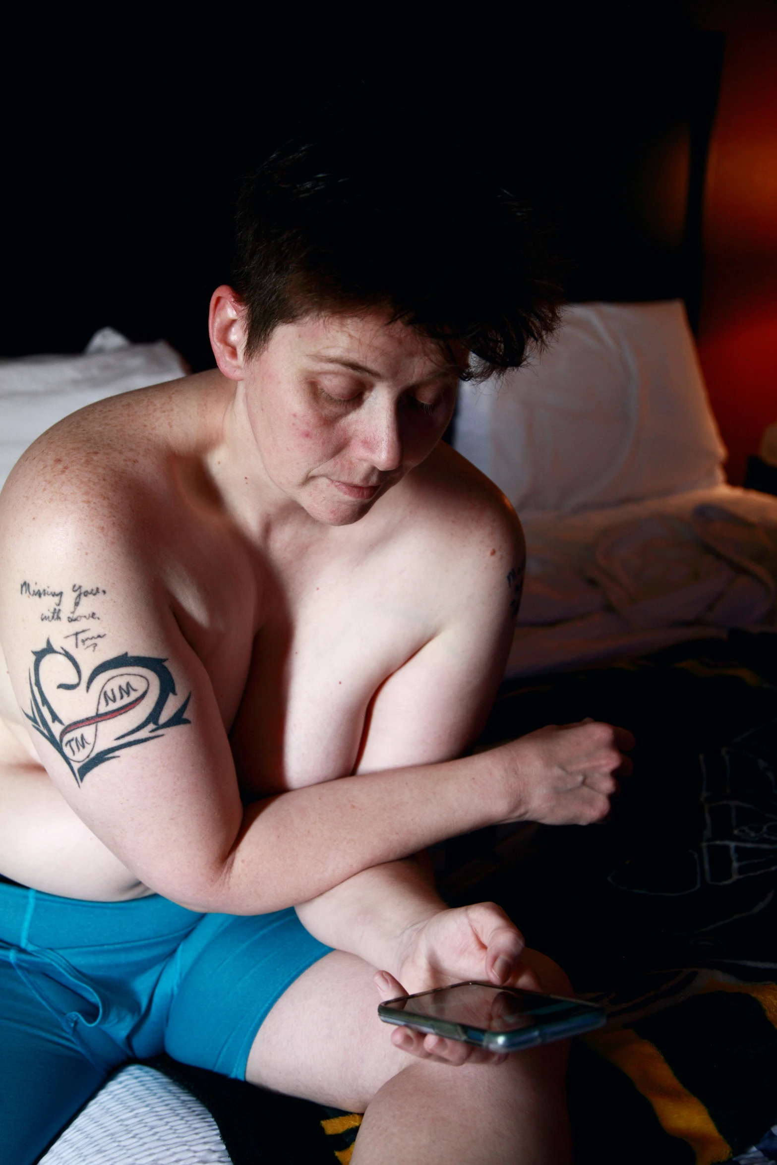 a man with a phone and tattoos sitting in bed