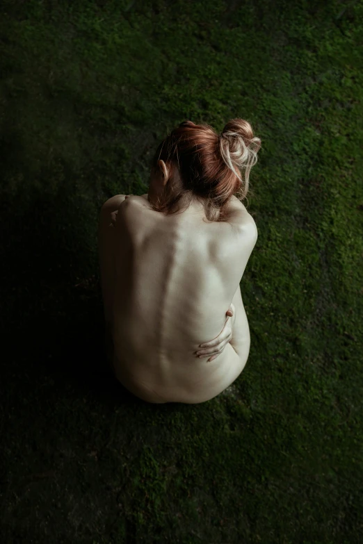 a  woman sitting in the grass staring down at the ground