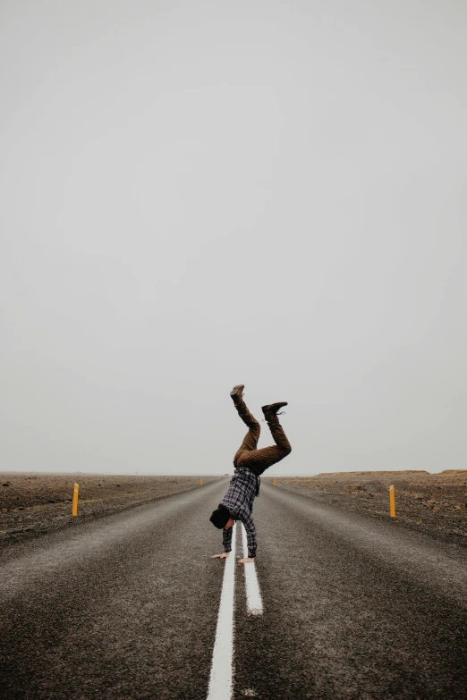 a man stands upside down in the middle of an empty road