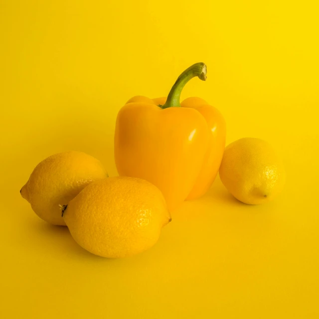 three lemons and one pepper are beside each other on a yellow background