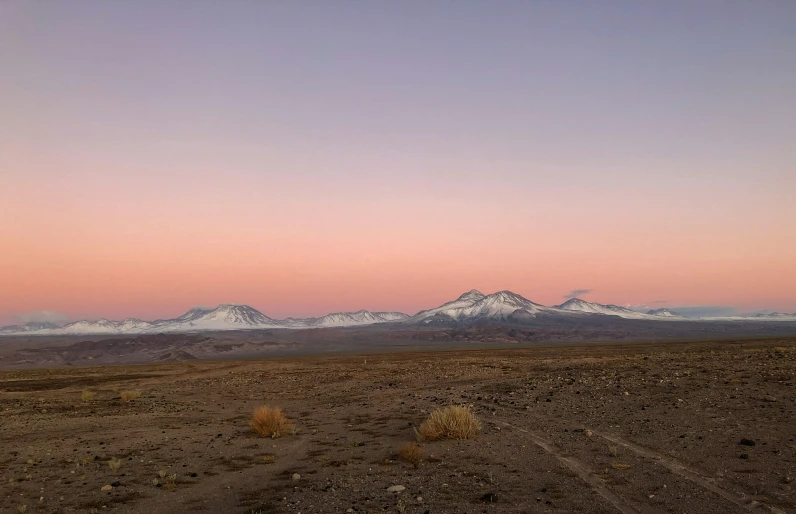 the sunset shines on an arid, dusty landscape with snow covered mountains in the distance