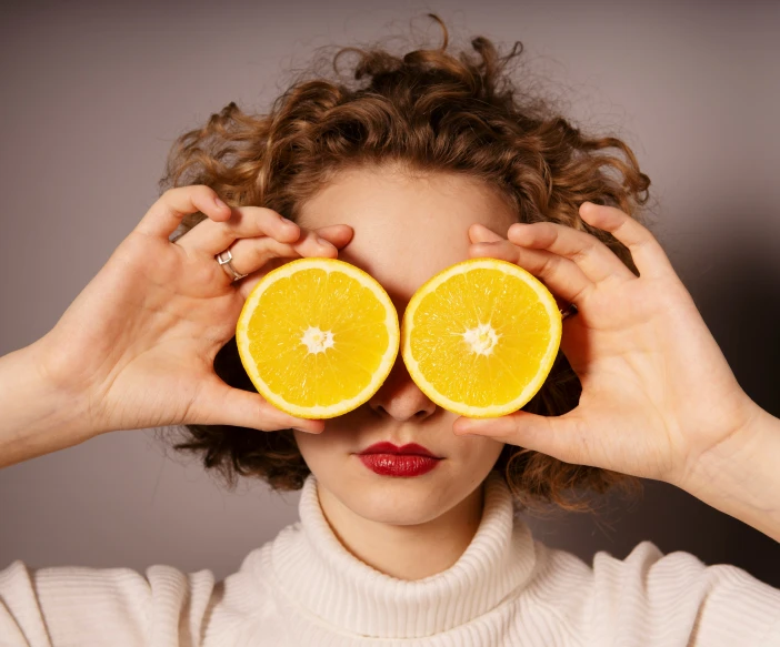 a woman holds halves of oranges up to their eyes