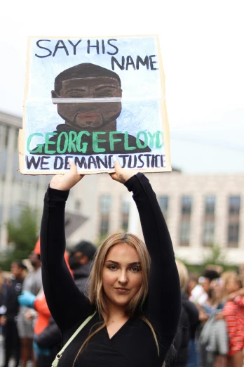 girl with black shirt holding sign in front of crowd