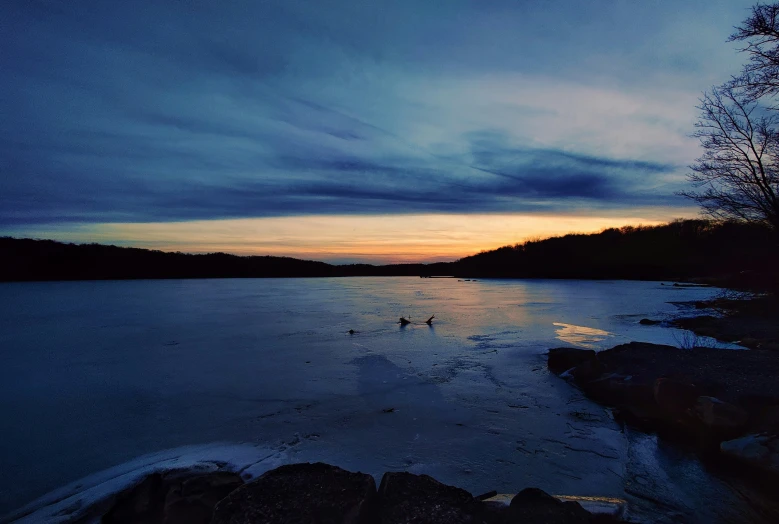 an evening view of water with two people wading