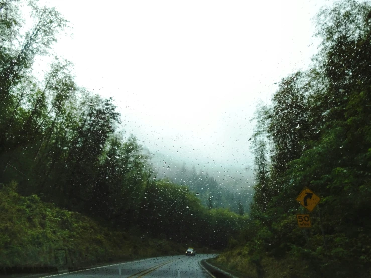 a rain soaked windshield is looking at a mountain road