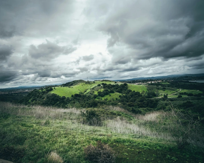 an area with green grass, a grassy hill, and cloudy sky