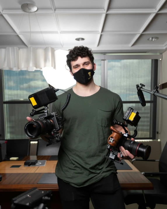 a man is holding two cameras while wearing a black mask